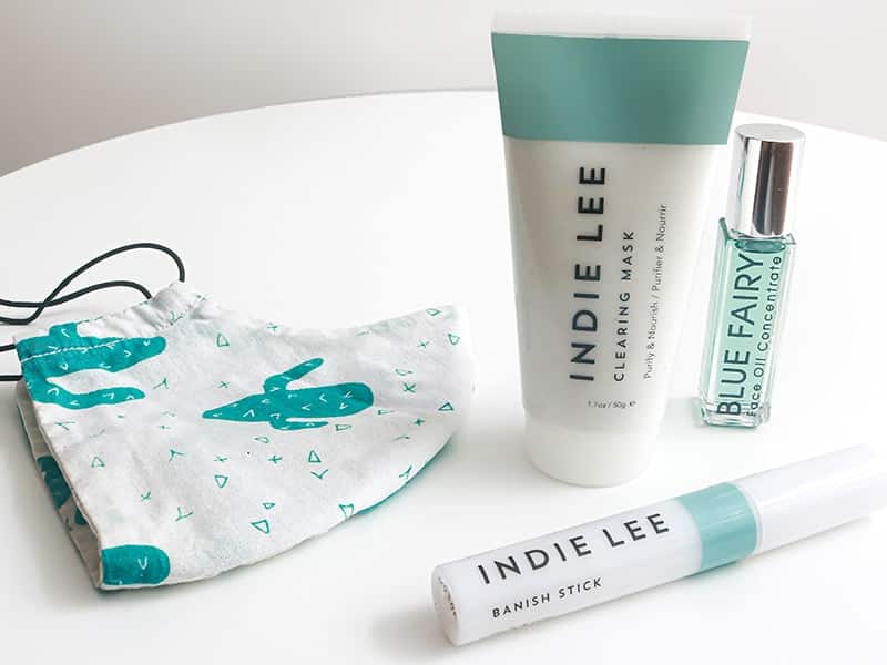 skin care routine for maskne featuring Indie Lee Clearing Mask, Indie Lee Banish Stick, Verdura naturalternative Blue Fairy Concentrate, and a cotton mask